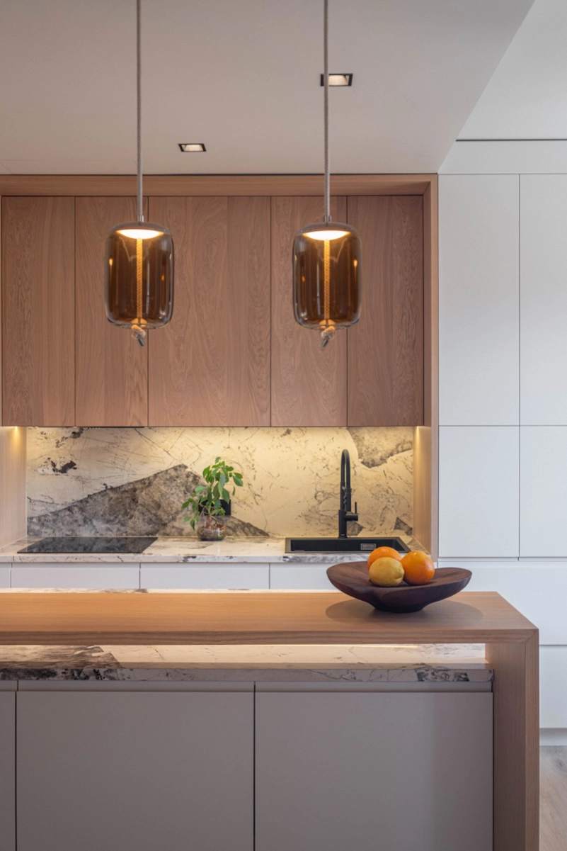 Cuisine design avec îlot central en bois, marbre veiné et suspensions décoratives – Projet L’Azur par Intérieurs à Croquer