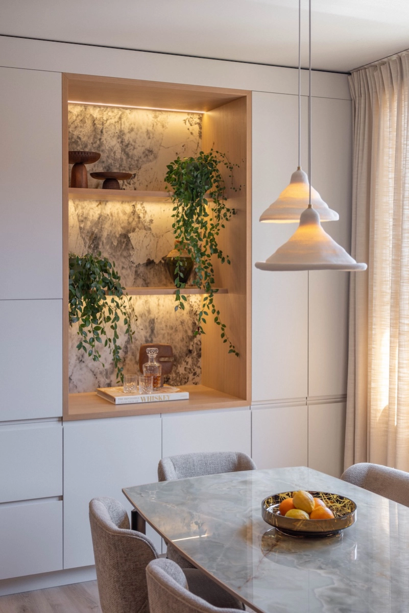Salle à manger contemporaine avec table en marbre, niche décorative éclairée et luminaires design – Projet L’Azur par Intérieurs à Croquer
